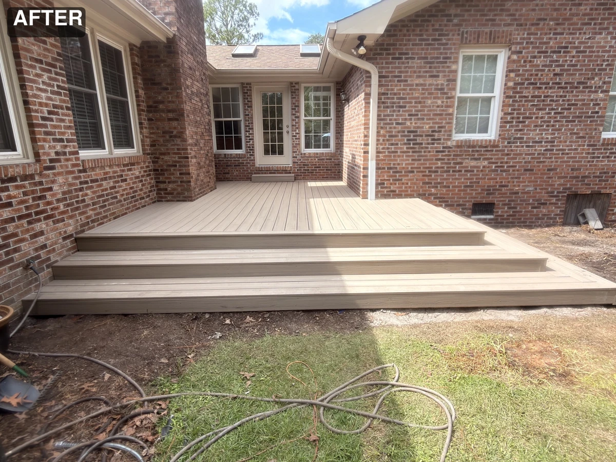 Completed light composite deck with broad steps beside a brick home